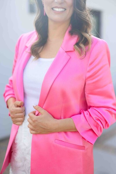 woman wearing vibrant pink blazer sharing authentic smile during professional headshot session with natural lighting