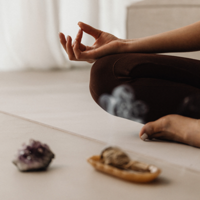 Close-up of a seated woman meditating beside healing crystals and burning incense, symbolizing spiritual connection, energy cleansing, and holistic wellness.