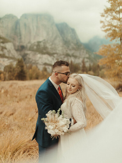 man and woman closely embracing with long veil in front of mountain views