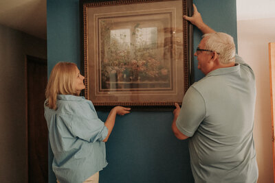 A touching moment of grandparents helping to hang a cherished picture during a family home session in Champaign, IL. Light By Zoey Photography documents everyday family life and connections in the Champaign-Urbana and Mahomet regions.