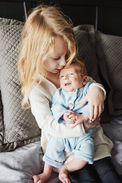 Sister holding baby brother during newborn session by Taylor Lynn Studios in Wheaton, IL