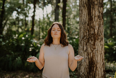 Intuitive raises hands while standing in the woods to meditate