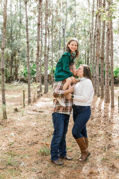 mom and dad kissing while daughter on daddy's shoulders