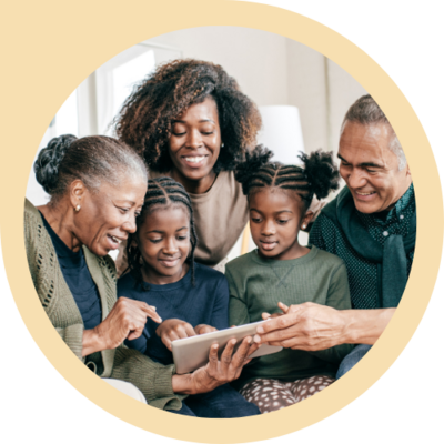 A mom and two grandparents surround a pair of adolescent siblings, looking down at a tablet together with loving smiles.