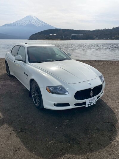 A black Ferrari California and a white Maserati Quattroporte parked side by side under the Tokyo expressway at Daikoku Parking Area, ready for a luxury drive experience.