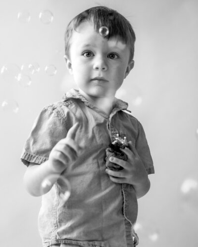 Boy popping bubbles while holding toy animals in studio in Annapolis Maryland.