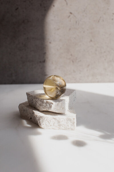 A citrine crystal sphere resting on quartz risers, on a marble surface with dappled light.