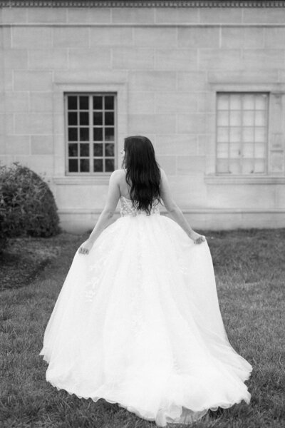 Bride in a strapless ball gown holding her dress, photographed from behind.