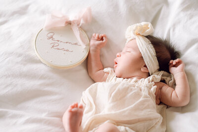 Newborn baby lying beside a name sign on a bed during a lifestyle session, captured by a Northern Virginia family photographer.