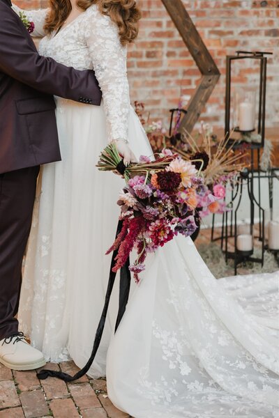 Bride holding large bouquet of colorful florals in purple, peach, pink and burgundy. Designed by New Jersey and Philadelphia floral designer, Jessamine Floral and Events.