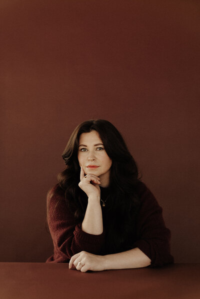 Classic headshot of Elisabeth Eden in a monochromatic burgundy color scheme, posing with her hand near her face, showcasing a modern and elegant personal brand style.