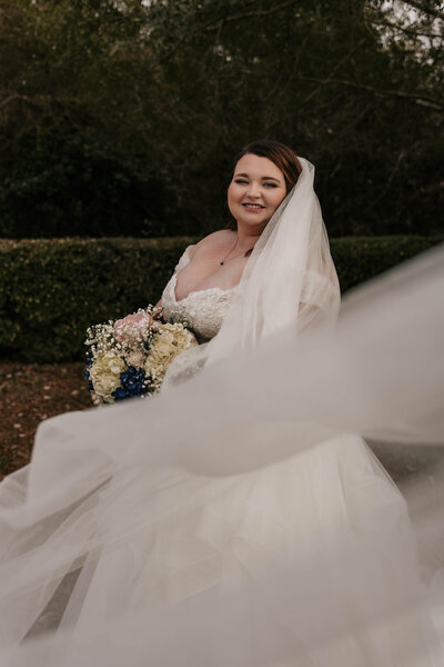 Bride smiles in her wedding dress with her veil blowing in the wind.