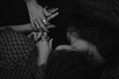 A couple rests in a field together and hold hands tightly.