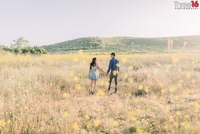 Engaged couple walk in an open field holding hands during engagement photos session on Quail Hill in Irvine