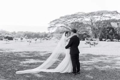 A newlywed couple with their arms around each other standing in a field 