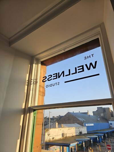The Wellness Studio branding sign on the window with the sun shining in.