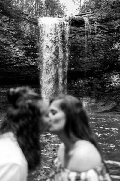 Adventurous lesbian couple kissing in front of georgia waterfall photographed by LGBTQ+ friendly wedding photographer