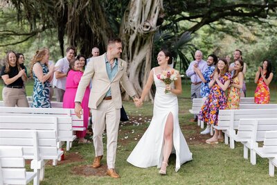 A wedding couple holding hands and walking back up the aisle 