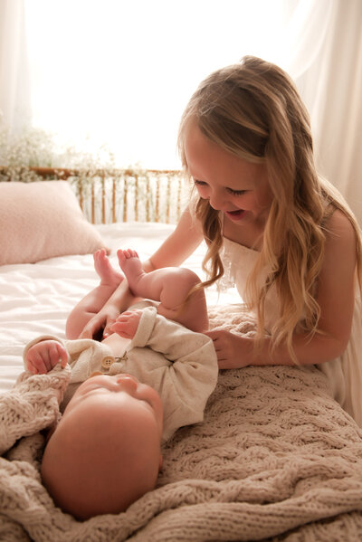 Big sister playing with her baby sibling who is laying on the bed in Hope's studio.