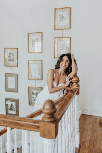 A bride leaning against a wooden railing smiles.