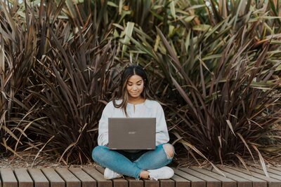 Student sitting criss cross with a laptop on their lap and head down. 