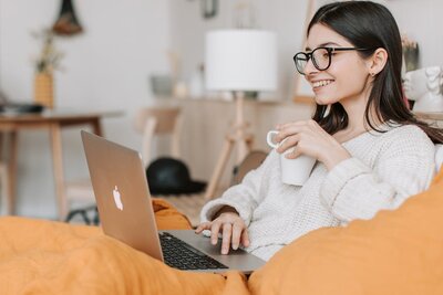 Woman in glasses sitting at a desk with a laptop and coffee mug representing ongoing virtual therapy sessions at Rooted & Nourished Psychotherapy
