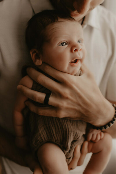 A dad holds his new son against his chest and the baby is awake