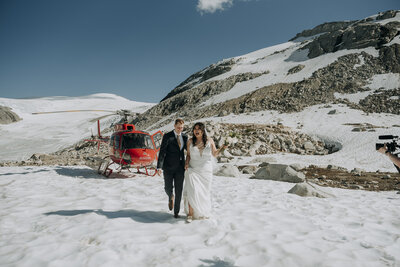 Bride and groom walk across snow from helicopter for their Whistler helicopter elopement ceremony at Ipsoot Glacier