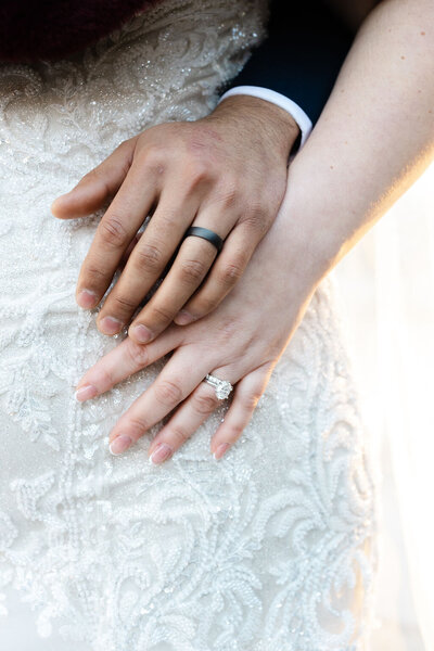 Close up of a bride and groom's hand on a lace wedding dress.