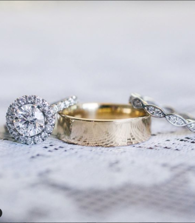 Close up photograph of man's wedding ring flanked by women's diamond wedding and engagement rings