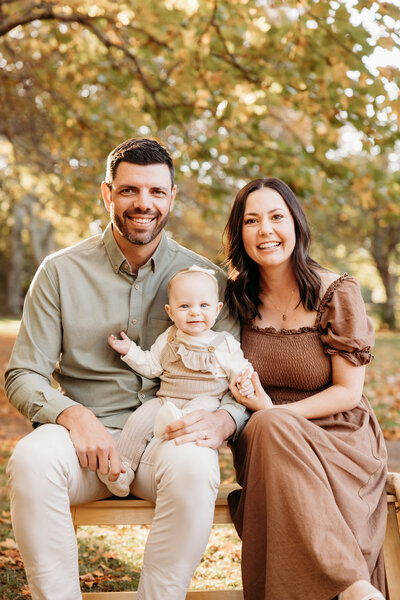 Chelsea and her husband holding their little baby girl during their autumn family photoshoot with michelle kelly at an auckland park