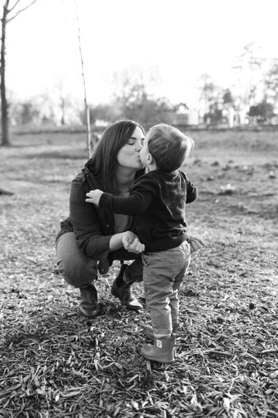 Black and white image of mom kissing toddler son at Nature Playscape in Forest Park