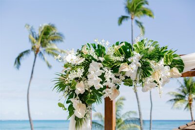 A white floral arrangement on the corner of a wooden arch 