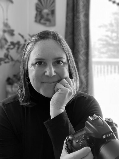 Self portrait of Jessica Uraneck, at her Freeport, Maine home, in black and white, with camera in hand.