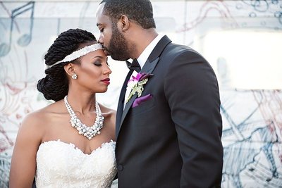 Groom kissing bride on forehead, bride is wearing a pearl statement necklace and headpiece