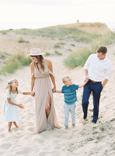 Family of four holding hands while walking on a beach