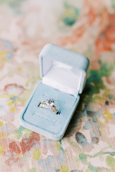 Close up image of wedding rings in a blue ring box sitting on colorful fabric