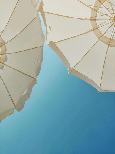 Looking up at two white beach umbrellas with blue sky behind them