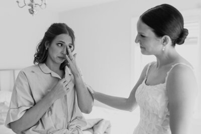 Black and white image of bride comforting sister while she is crying