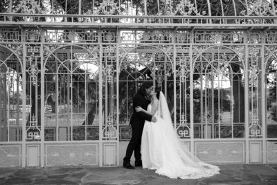 An Austin-based wedding photographer captures a tender moment as a bride and groom kiss in front of an ornate greenhouse.