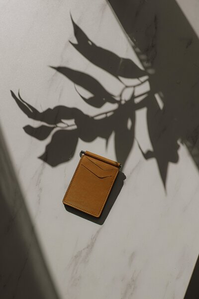 Tan Wallet lying on a marble bench with the shadow of a plant cast over it