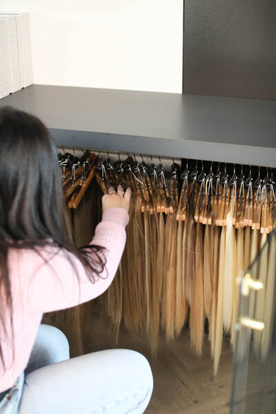 calgary hairstylist looking through row of IBE Invisible Bead Extensions hanging on a rack at a hair salon in calgary alberta