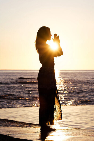 Fanny de Pause Prana de profil, mains jointes face à son visage, coucher de soleil sur la plage.