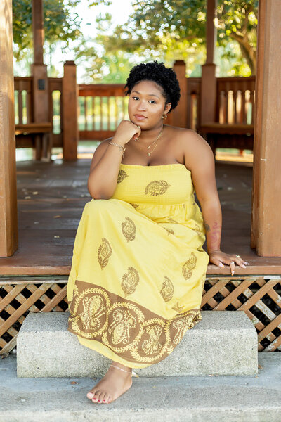 African American woman in yellow sundress sitting on gazebo steps