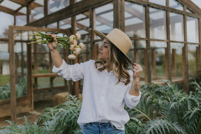 Peaches and Poppies Floral owner holding up flowers and smiling at them in her greenhouse