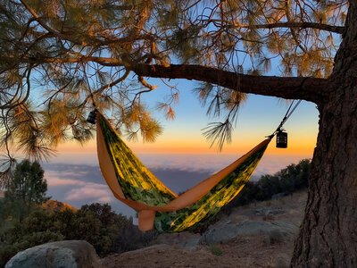 A hammock suspended between trees with a breathtaking Pacific and mountain sunset view, part of a curated luxury outdoor retreat