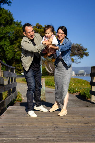A joyful family playing with their toddler on a wooden boardwalk by the Bay – ellobelle photography.