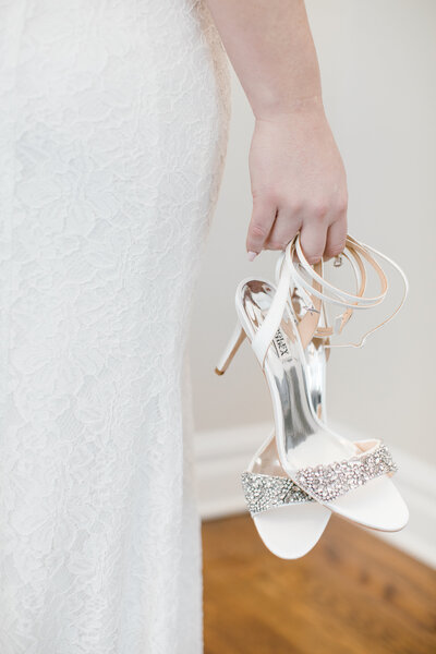 Bride Holding designer bridal shoes in one hand with arm down by her side