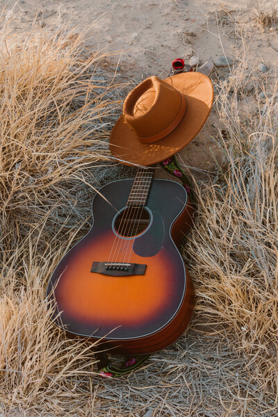 A western-inspired lifestyle flat lay featuring an acoustic guitar and a wide-brimmed cowboy hat resting in dry grass during a creative branding session in Big bend in West Texas.