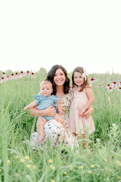 Mom smiling with her two daughters in a field of flowers.
